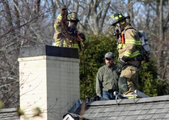 Camden firefighter Bob French Jr. chains smoldering debris down the chimney while Ryan Fisher looks on. (Photo by Holly S. Edwards)