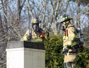 Camden firefighters Bob French Jr. and Ryan Fisher on the roof clearing a chimney fire at 26 High St. Thursday morning. (Photo by Holly S. Edwards)
