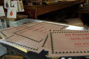 Signs advertising specific discounts for Saturday morning's Early Bird sale arrayed on the counter at Out of the Woods, a shop specializing in Maine-made products (Photo by Wes Sterrs)