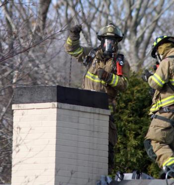 Camden firefighter Bob French Jr. uses a balled-up bunch of chain to clear a smoldering fire and debris from inside a chimney at 26 High St. Thursday morning. (Photo by Holly S. Edwards)