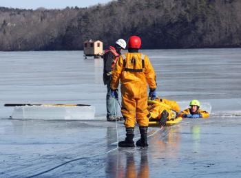 Firefighter Brian Sullivan makes his way atop the ice rescue sled toward Mike Cole, in the water. (Photo by Holly S. Edwards)