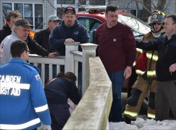 Tracy Harford, in burgundy, reaches Knowlton Street from the edge of the Megunticook River mill pond Friday afternoon. (Photo by Lynda Clancy)