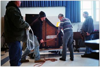 BELFAST - A baby grand piano donated by local businessman Bruce Starrett arrives at Belfast Area High School. Music teacher John Cameron, striped shirt, said new instrument will allow for piano duet recitals without moving a third piano belonging to the school off the auditorium stage for each performance. BELFAST - A piano donated by Bruce Starret arrives at Belfast Area High School. Music teacher John Cameron, striped shirt, said new instrument will allow for piano duet recitals without moving a third piano off the auditorium stage each time. (Photo by Ethan Andrews)