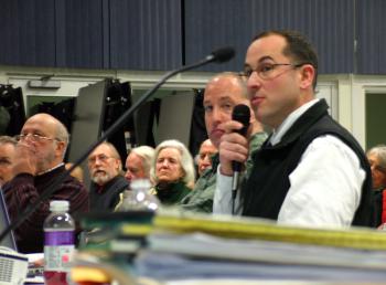 Mike Lucy, with microphone, and Frank Gallagher, behind Lucy, of the security risk consulting firm Good Harbor, detail their company's report to the Searsport Planning Board and roughly 200 people in attendance at a public hearing on Monday night (Photo by Ethan Andrews)