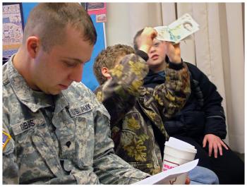Justin Gibbs of Stockton Springs, left, a veteran of the Iraq War brought his grandfather's WWII uniform to the presentation at Captain Albert Stevens School. Behind Gibbs, students inspect a stack of old European and British currency. (Photo by Ethan Andrews)
