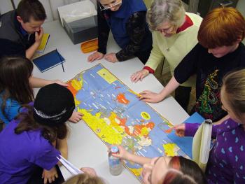 Students from the Captain Albert School in Belfast crowd around a geopolitical map of World War II after a presentation by Belfast Historical Society & Museum Director Megan Pinette, top, center. Meg Hunter, next to Pinette, recalled being a young girl in London during German air raids. (Photo by Ethan Andrews) Fourth and fifth grade students from Captain Albert School in Belfast crowd around a geopolitical map of World War II following a presentation at the school by Belfast Museum and Historical Society Director Megan Pinette, top, center. (Photo by Ethan Andrews)
