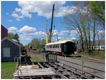 A former Belfast and Moosehead Lake Railroad passenger coach is moved into place to be loaded by crane onto a waiting flatbed rail car visible further down the track. (Photo by Ethan Andrews)