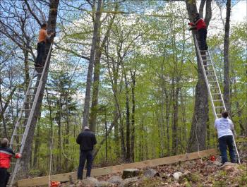 Camden firefighters Eric Verite and Andrew Lowe climb the ladders, while Chief Chris Farley, Cheyne Hansen and Camden First Aid's Brian Allen prepare to hoist the beam into place high in the trees. Competitors in the first-ever Run For Your Life obstacle course race will be climbing ropes to the top of the beam. (Photos by Lynda Clancy)