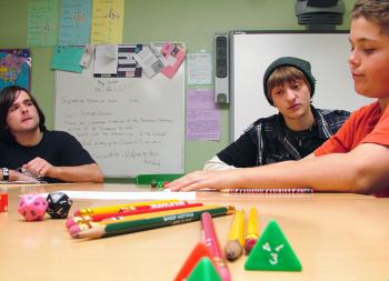 Stephen Colby, center, advises Casey Baxter, right, in a game of Pathfinder during a weekly session hosted by the Game Loft at Mount View Middle School. Colby, a longtime member of the Belfast-based after school program built around non-electronic gaming. Mount View student Tyler Cross, left, would later take over for Colby to lead a younger group. (Photo by Ethan Andrews)