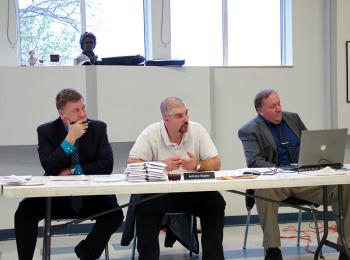 RSU 20 Superintendent Brian Carpenter, left, school board chairman Anthony Bagley and Assistant Superintendent John McDonald listen to testimony opposing proposed staff and teacher cuts, May 15. The stack of envelopes on the table holds letters from students at Troy Howard Middle School supporting the school's visual art program whose sole teacher is on a list of positions to be cut next year. (Photo by Ethan Andrews)