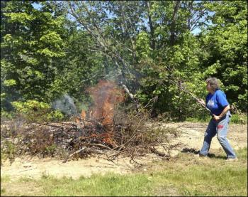 Diane O’Brien, chairman of the Lincolnville Historical Society, throws brush on the fire while helping to clear land for the society’s open-air museum next to the new library. (Photo by Sheila Polson)