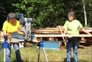 Diane O’Brien, chairman of the Lincolnville Historical Society, and Laurel Ames saw lumber for the floor joists on the open-air museum sheds. (Photo by Sheila Polson)