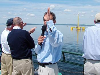 Dr. Habib Dagher, center, of the University of Maine's Advanced Structures & Composites Center, speaks during press conference Thursday marking the ceremonial connection of the first offshore wind turbine in the United States — a 65 foot tall, 1:8 scale prototype, background — to the mainland electrical grid. (Photo by Ethan Andrews)