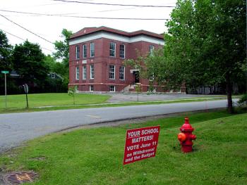 A sign put out by supporters of a six-town movement to withdraw from the consolidated Regional School Unit 20 stands outside the former Peirce Elementary School in Belfast, a casualty of a previous consolidation. Municipalities around the state go to the polls on June 11 to validate local school district budgets. Some will have additional questions to reckon with. (Photo by Ethan Andrews)