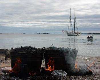 The schooner ‘Mary Day’ sits anchored off Lobster Island while a lobster bake feast steams away on the beach and passengers and crew are rowed ashore. (Photo by Holly S. Edwards)