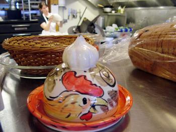 At the recently re-opened Monroe General Store, Becca Biggs tosses pizza dough for the store’s Wicked Rooster Café. In the foreground, a garlic roasting dish by local potter and store employee Bill Davis. The depiction of a rooster on the dish was coincidental, he said. (Photo by Ethan Andrews)