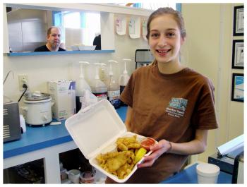 Natalie Nugent shows a combination dish called “The Big 3” at Off the Hook Shuckin’ Shack. In the background, Chef Wayne Cousins prepares the next order. (Photo by Ethan Andrews)