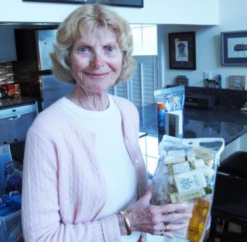 Judy Beebe holding up the school kits they deliver, which contain donated bottles of mini shampoos and conditioners from hotels, among other items. (Photo by Kay Stephens)