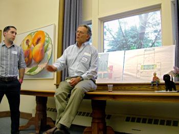 Jim Curry, center, talks to a group of 25 people at the former Crosby School in Belfast about selling the building. Curry and Chris Yedibalian, left, represented National Theater Workshop of the Handicapped, the owner and most recent occupant of the building. At right are floor plans and a figurine of NTWH founder Brother Rick Curry. (Photo by Ethan Andrews)