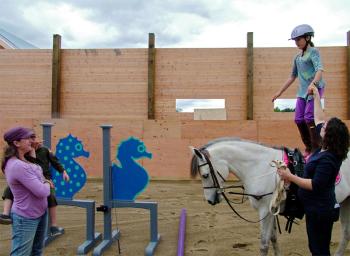 Seahorse Stables owner Amy Miller, left, watches as her daughter Nina tries some vaulting moves with help from trainer Jessica Pilley. (Photo by Ethan Andrews)