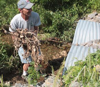 Camden Snow Bowl employee Carl Sager removes debris from the culvert that allows Hosmer Brook to travel under the gated entrance and into Hosmer Pond. (Photo by Holly S. Edwards)