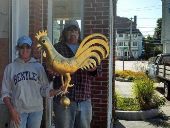 Camden Parks and Recreation crew members Richelle Gagne and John Gould pose with the gold-leaf rooster that was left in the bed of their work truck earlier in the morning Sept. 10. The rooster, which tops one of two weathervanes on the gatehouses at the entrance to the Camden Public Library Amphitheatre, was reported stolen Monday morning. (Courtesy Camden Police Dept.)