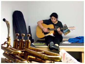 After performing on trombone earlier in the evening, Dany Wilson plays guitar in a corner of the band storage room. (Photo by Ethan Andrews)