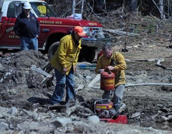 From left, Searsmont Asst. Chief Wayne Woodbury, First Lt. Joel Cox and Liberty Fire Chief Bill Gillespie. Cox and Gillespie place a floating pump in standing water to deliver the water deep into the woods. (Photo by Holly S. Edwards)