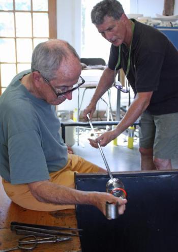 David Jacobson spins the punty on the rail, while Richard Anderson uses a jack to shape the sides of his drinking glass. (Photo by Holly S. Edwards)