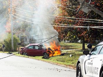 It did not take long for the fire inside the engine compartment of Kevin Curit’s 2014 Dodge Dart to burn in earnest Monday afternoon, after he went off the road, became airborne, shattered a utility pole, possibly rolled in midair, and came to rest facing the wrong way from where he came. (Photo by Holly S. Edwards)