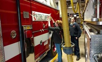 Rachel Pette of Adventure Advertising in Rockport works with Matt Heath, firefighter, to secure one of the winning logo banners on Camden’s ladder truck. (Photo by Chris Farley)