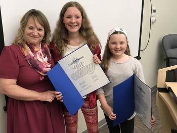 From left, Dorothy Havey, special assistant to Senate President Michael Thibodeau, with Isabella and Maren Kinney during Monday night’s Lincolnville Board of Selectmen’s meeting, at which the Kinney sisters were honored with a Legislative Sentiment and learned that the 2017 Town Report had been dedicated to them for their role in saving a life – their father, Town Administrator David Kinney. (Photo by Holly S. Edwards)
