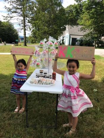 Kaidi (left) and Kaida Nguyen hold signs to promote their fundraiser for MCH Meals on Wheels, at KK’s Corner, the name of their fundraising spot at Tropical Nails in Rockport. (Photo courtesy of Tracie Nguyen)