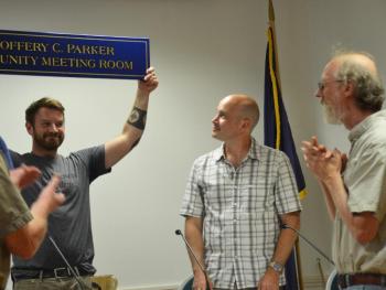 Rockport Select Board member Owen Casas proudly holds the new sign that designates the opera house meeting room as the Geoffrey C. Parker Meeting Room. Select Board member Tom Gray stands to the left of Casas, as Parker gets surprised by the citizen gesture.