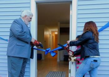 Brandi Brown (right) cuts the ceremonial ribbon with the help of Randy Mailloux, the board president of Habitat for Humanity of Waldo County. (photo by Erica Thoms)