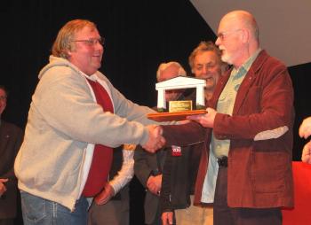 Former Camden Select Board Chairman John French shows that town business is not always conducted while sitting behind the table at the Washington Street Conference Room. In February 2016, at Rockport’s 125 Celebration, French presented Rockport Select Board Chair Bill Chapman with an award for winning the first-ever toboggan competition between the two towns. (Photo by Chris Wolf)