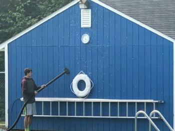 A lifeguard vacuums the moths off of a Belfast City Pool storage building. (photo courtesy Belfast Police Sergeant John Gibbs.)