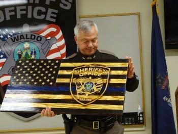 Trafton poses with a gift given to the sheriff’s office by him and his wife Wendy. The gift was commissioned by a veteran who creates wooden flags.(photo by Erica Thoms)
