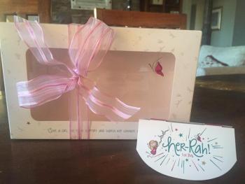 Packaging for the gift set in background; retail store identification in front. Her-Rah! First Bra