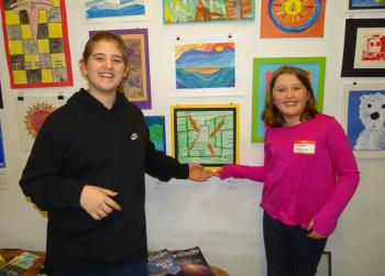 Searsport fourth grader Amelia Seekins stands with her friend and classmate Cara in front of Cara’s artwork. (photo by Erica Thoms)