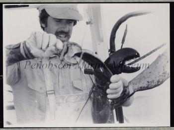"Lobsterman David Cousens, of South Thomaston, Maine, demonstrates how he places a colored band down over one of the claws of a female lobster he catches before they are released into the sea. It is slipped over the large claw and attached around a lower knuckle so that it does not interfere with feeding. When the lobster is caught again, Dave can recognize it as one he has already recorded in the Maine Agricultural Experiment Station study." (No attribution; if you have information about the photographer, please contact Penobscot Marine Museum. (207) 548-2529)