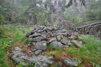 This large cairn occupies a flat area at the top of Ducktrap Mountain. It appears to be part of a grouping of stone structures aligned in a linear arrangement, including two large stacked stone structures, as well as a natural formation which has been used as a fire pit or altar in the past.
(Photo courtesy Dennis Cerrotti)