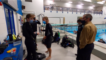 Prior to entering the water and to keep masks from fogging, BAHS Marine studies students Izik Marriner, Jesse Cowan and Paige Rollerson apply some de-fogger to their masks from Aqua Diving Academy dive master, while Marine Studies teacher Dave Thomas looks on. (Photo by Charles H. Lagerbom)