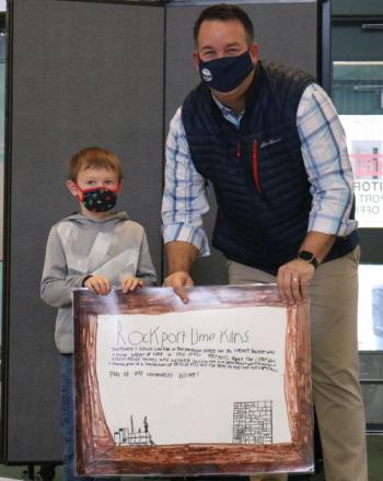 Third Grader Finn Hedstrom, of Lynda Pierce's class, presents his class poster to Rockport Town Manager Jon Duke highlighting the history of the Lime Kilns at Rockport Harbor.
