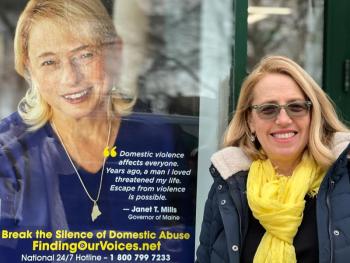 The first Janet T. Mills Finding Our Voices business-window banner to be posted in Maine, at the Camden Town Office.
Patrisha McLean with the first banner featuring Maine’s Governor Janet Mills, now hanging in Camden. “Camden is where the banner campaign launched, at the start of COVID in April 2020,” said McLean. “Then, we were 20 survivors on banners. Now, with Janet T. Mills, we are 40.”