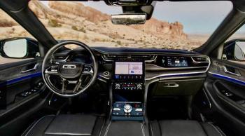 The Grand Cherokee Overland cockpit. The two tabs flanking the gearshift knob, below the center console, select the drive mode and the ride height. Note the third screen in front of the passenger.