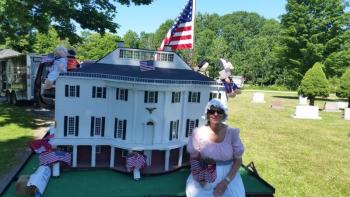 Volunteer Sally Williamson, in period costume, sits along a miniature replica of the Knox Museum. (Photo by Sarah Shepherd)
