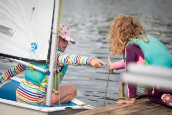Summer sailing students work together to tie up an Opti at the dock. (Photo by Christine Canella)