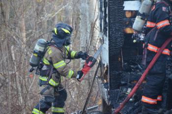 Camden firefighter Matt Heath uses a chainsaw to access smoldering interior boards of the building. (Photo by Lynda Clancy)