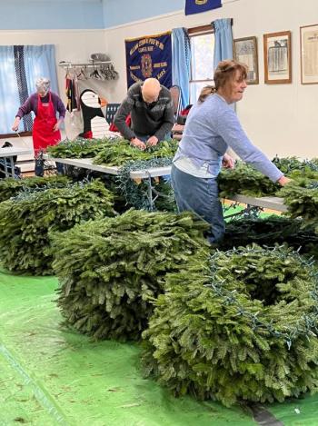 Members of Camden Garden Club painstakingly fix loops of lights to downtown lamppost wreaths. (Photo courtesy Camden Garden Club)